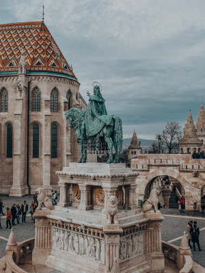 Imagem de uma das diversas praças de Budapeste, com o monumento de uma pessoa em cima de um cavalo, por cima de outras esculturas em mármore.